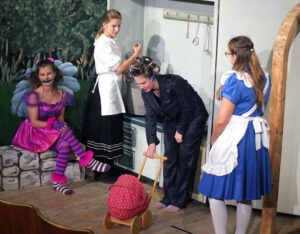 Alice gelangt in eine Küche, wo eine Grinsekatze sitzt, eine Köchin hauptsächlich mit Pfeffer kocht und ein Kind sich in ein Schweinchen verwandelt. © G. Prantl